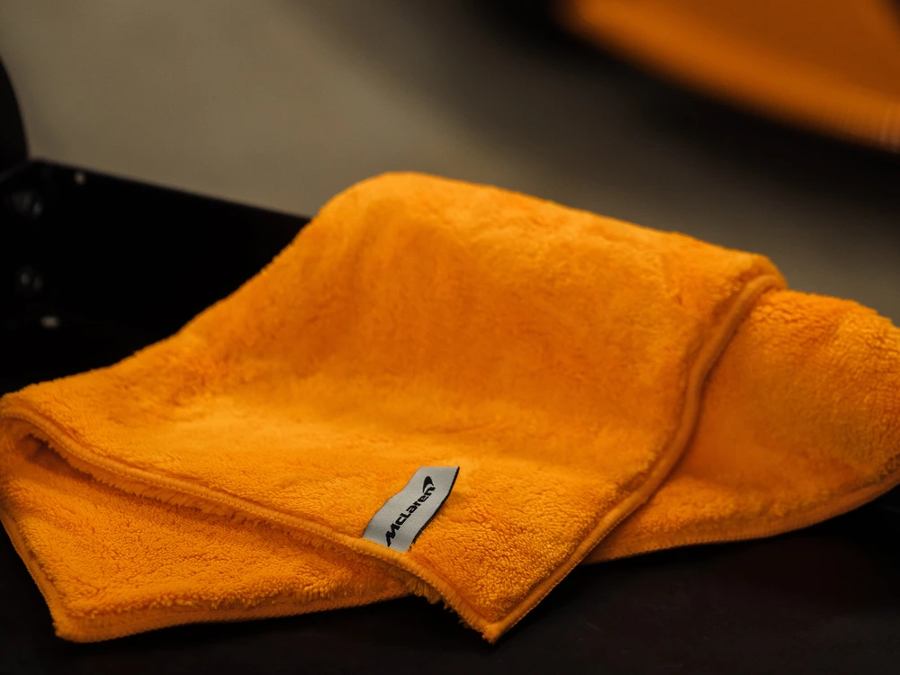 Serviette McLaren Luxury Microfiber sur un plateau devant une McLaren orange