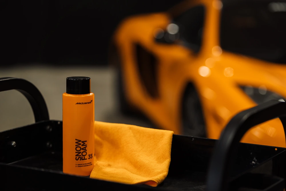 Bouteille McLaren Snow Foam avec microfibre orange devant une McLaren