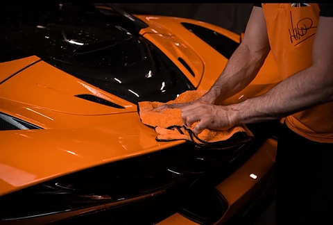 McLaren orange nettoyée à la main avec une microfibre orange dans l'atelier