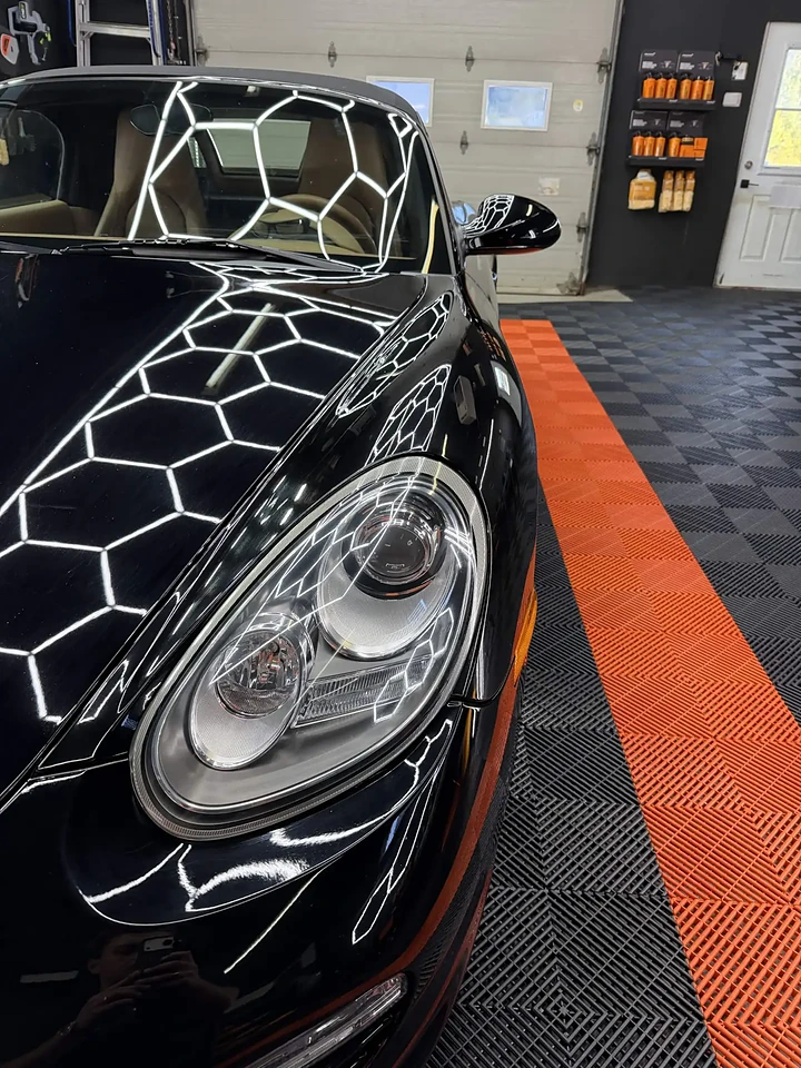 Porsche noire cabriolet dans l'atelier Prestige, phare mis en évidence sous l'éclairage hexagonal